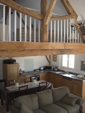 A loft-style kitchen with exposed wooden beams, a dining area with a table and chairs, and a sofa in the foreground. - Charming vacation rental, ideal for visiting Chambord, Cheverny, and Beauval—2 air-conditioned bedrooms (Fontaines-En-Sologne)