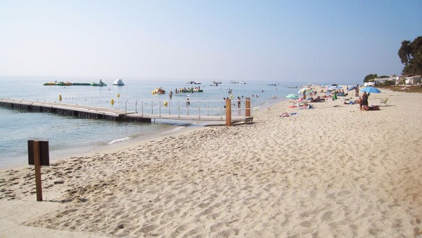 A beach with a pier extending into the water, people relaxing on the sand, and boats in the distance. - Quiet chalet, between sea and mountain (Isolaccio-Di-Fiumorbo)