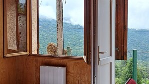 A wooden cabin room with a bed, a window with a view of mountains, and a door leading outside. - Quiet chalet, between sea and mountain (Isolaccio-Di-Fiumorbo)