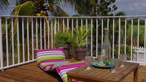 A wooden deck with a white railing, a striped sofa with pillows, potted plants, and a table with glasses and a bottle. - "Lisoé Lodge, a stone's throw from the sea  (LE MOULE)