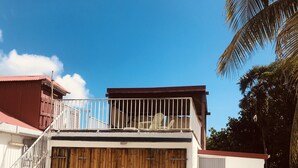 A two-story building with a wooden door, a balcony with a railing, and a tiled patio area. - "Lisoé Lodge, a stone's throw from the sea  (LE MOULE)