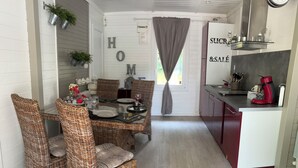 Un comedor con sillas de mimbre y una mesa preparada para cuatro, una cocina con una cafetera roja y un letrero que dice 'HOME' en la pared.