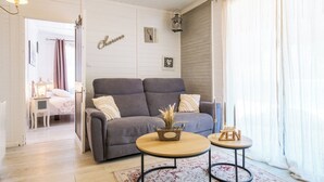 Una sala de estar con un sofá gris, dos mesas redondas, una mesita auxiliar y una cama al fondo.