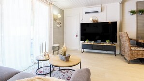 Una sala de estar con un sofá, una mesa redonda de centro, un televisor y una silla de mimbre.