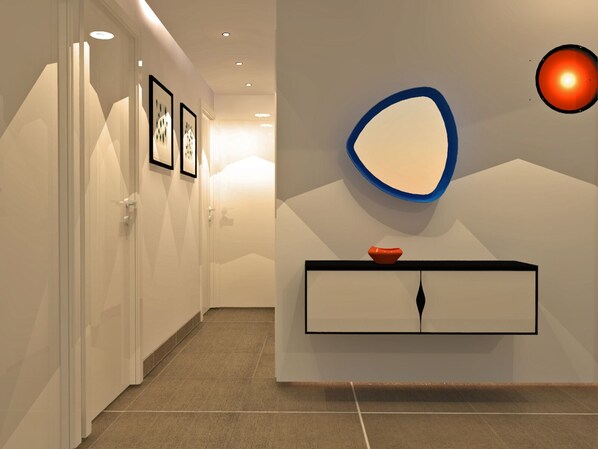 A modern hallway with a white door, framed pictures, a wall-mounted mirror, and a black console with a red bowl. - Appart. 75 m2 2 bedrooms location facing the sea and in the heart of Palavas (Palavas-Les-Flots)