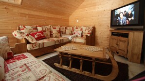 Interior acollidor d'una cabana de fusta amb un sofà de fusta, una taula de cafè i una televisió sobre un moble de fusta.