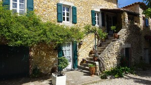 A stone building with green shutters, a staircase, and potted plants.