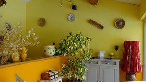 A room with yellow walls, wooden ceiling beams, a white chair with blue stripes, a white table, and a potted plant.