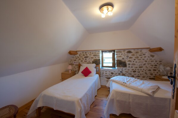A small, cozy bedroom with two beds, a stone wall, a wooden ceiling, and a window. - Beautiful countryside, 5 min walk from all amenities (Susmiou)