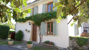 A quaint house with a wooden door, green shutters, and a stone pathway leading to the entrance.