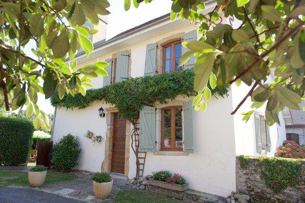 A quaint house with a wooden door, green shutters, and a stone pathway leading to the entrance.