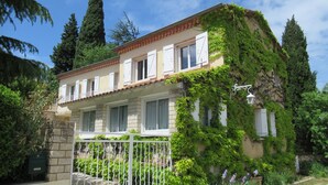 A two-story house with a balcony, surrounded by greenery and a gated entrance. - Charming house in Provencal Gard, large garden, swimming pool, children's games (Orsan)