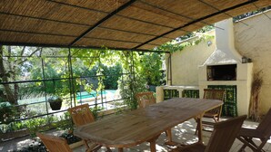 An outdoor patio with a wooden table and chairs, a grill, and a view of a swimming pool. - Charming house in Provencal Gard, large garden, swimming pool, children's games (Orsan)