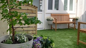 Un pequeño patio trasero con cerco de madera, un banco de madera y plantas en macetas.
