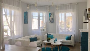 Una sala de estar moderna con sofás blancos, cojines verde azulado y una mesa de centro de madera.
