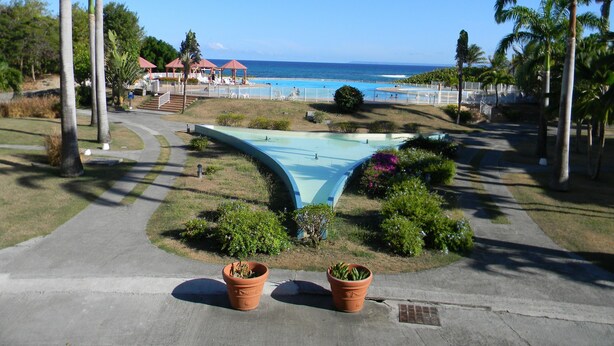 A pool area with a curved water feature, surrounded by palm trees and a view of the ocean. - Apartments in Saint-Francois (SAINT FRANCOIS)