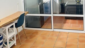 A room with a sliding glass door leading to a kitchen area, a wooden table with a chair, and a bed with a striped bedspread. - Apartments in Saint-Francois (SAINT FRANCOIS)