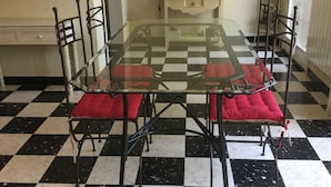Ein Essbereich mit einem Glastisch, umgeben von Metallstühlen mit roten Kissen. Der Boden hat ein schwarz-weiß Karomuster.