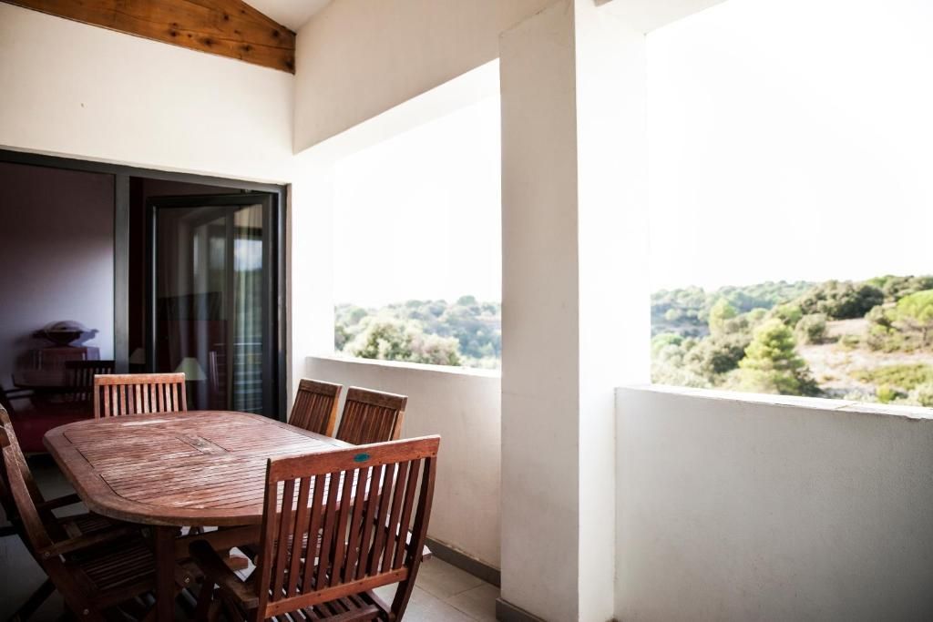 A balcony with a wooden table and chairs, a sliding glass door, and a view of a hilly landscape.