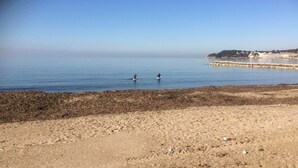 A beach with two paddleboarders in the water, a sandy shore, and a distant shoreline with buildings.
