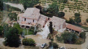 A large, two-story house with a tiled roof, surrounded by a garden and a vineyard.