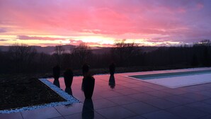 A swimming pool with a tiled deck and a view of a sunset over a forested landscape. - Bright architect-designed house-private saltwater pool-wonderful unobstructed view (Le Bugue)