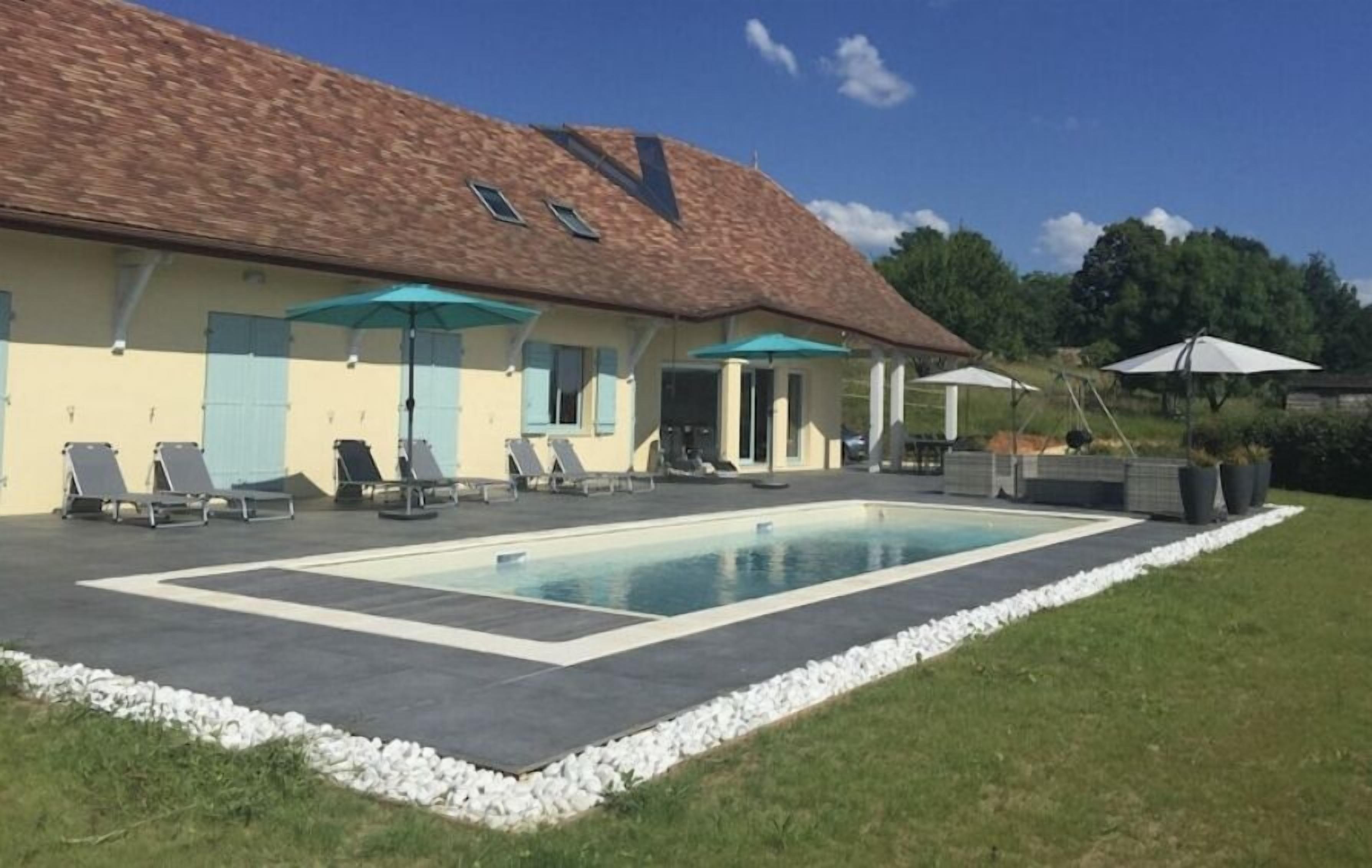 A building with a swimming pool, outdoor seating, and umbrellas.
