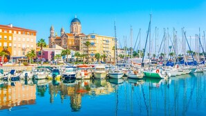 Una marina con numerosos barcos amarrados, una iglesia destacada con cúpula y edificios coloridos a lo largo del paseo marítimo.