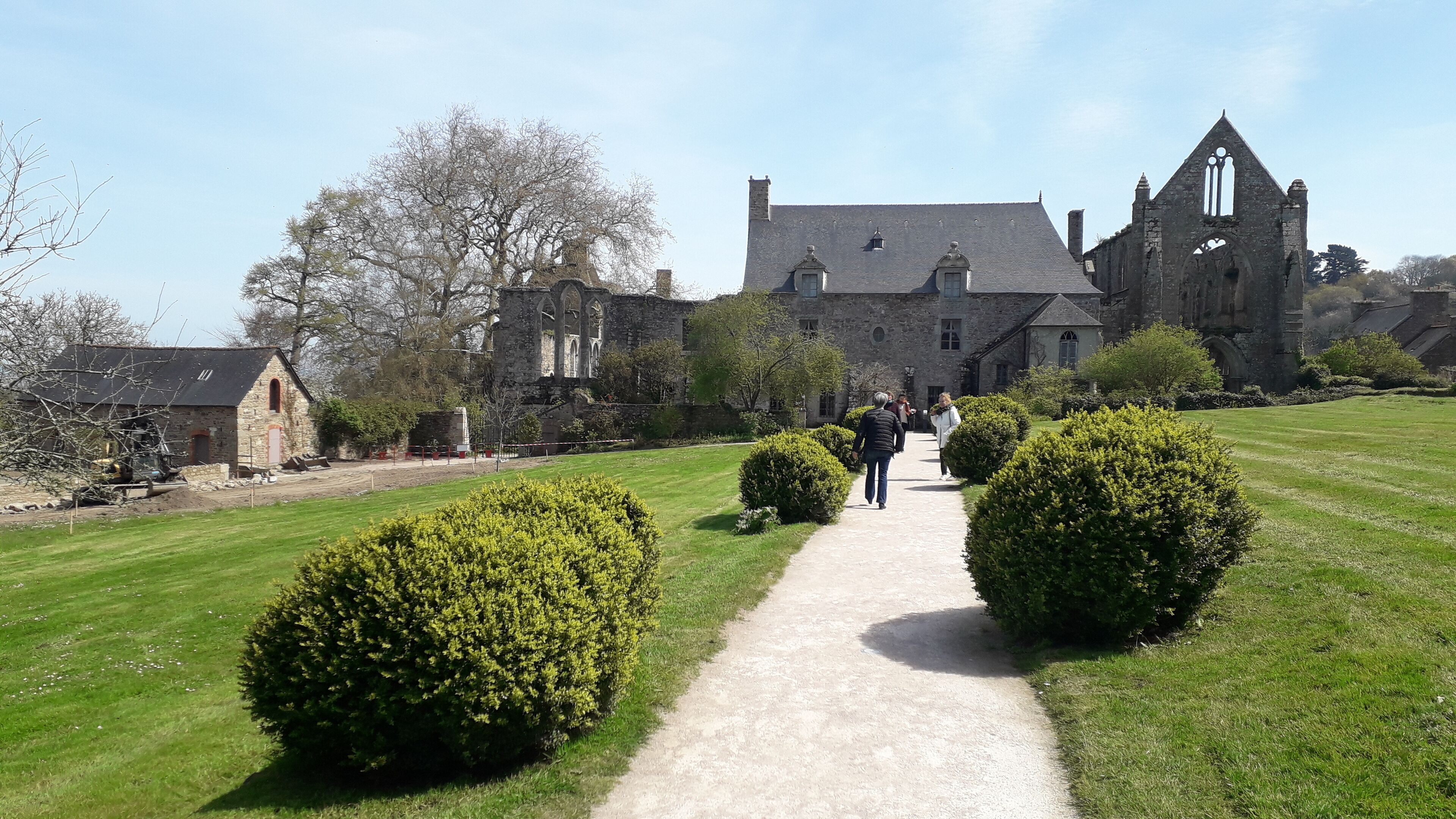 A historic stone building with a central courtyard, a gravel path, and well-maintained hedges.