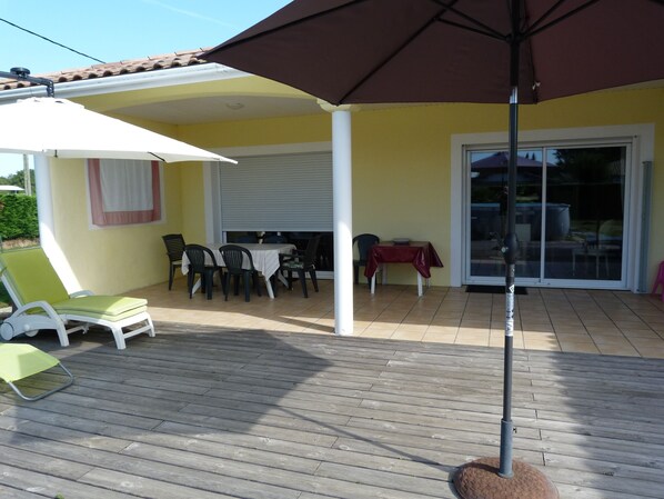 A covered patio with a table and chairs, a sliding glass door, and a wooden deck.
