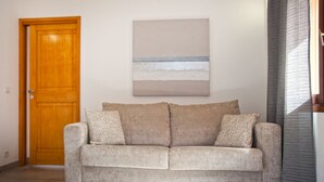 A beige sofa with patterned cushions in a room with a wooden door and a painting of a beach scene on the wall. - MONTE-CINTO Stone house -PAGLIAGHJU- Gorges de l'Asco, not far from the sea  (Moltifao)