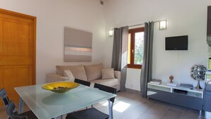 A modern living room with a glass dining table, a sofa, a TV, and a window with curtains. - MONTE-CINTO Stone house -PAGLIAGHJU- Gorges de l'Asco, not far from the sea  (Moltifao)