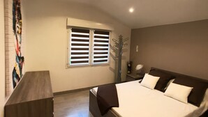 A bedroom with a bed, a nightstand, a dresser, a window with blinds, and a wall-mounted sign. - Villa with swimming pool, large terrace, all comfort, enclosed garden, calm. (Forcalqueiret)