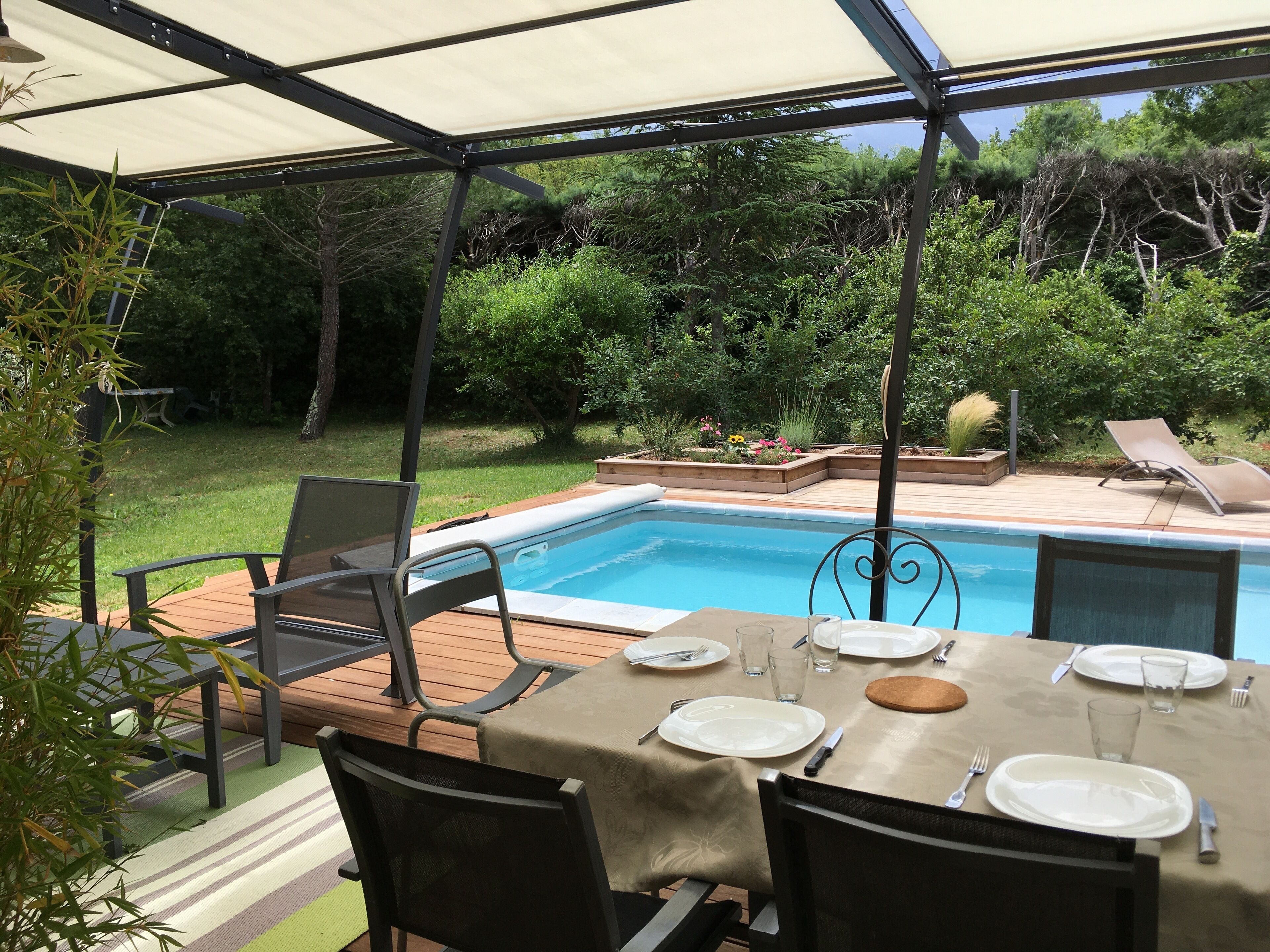 A covered outdoor area with a pool, dining table, chairs, and a table set for a meal.