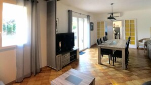 A spacious living area with a wooden ceiling, a dining table with chairs, a television, and a sliding glass door leading to a balcony. - Villa with swimming pool, large terrace, all comfort, enclosed garden, calm. (Forcalqueiret)