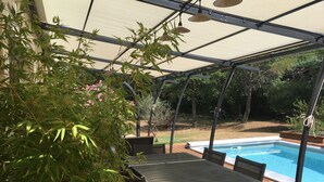 A covered patio area with a pool, wooden deck, and outdoor furniture. - Villa with swimming pool, large terrace, all comfort, enclosed garden, calm. (Forcalqueiret)