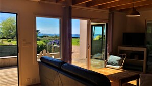 Een moderne woonkamer met een grote schuifpui die uitkomt op een terras, een bank, een televisie en een houten tafel.