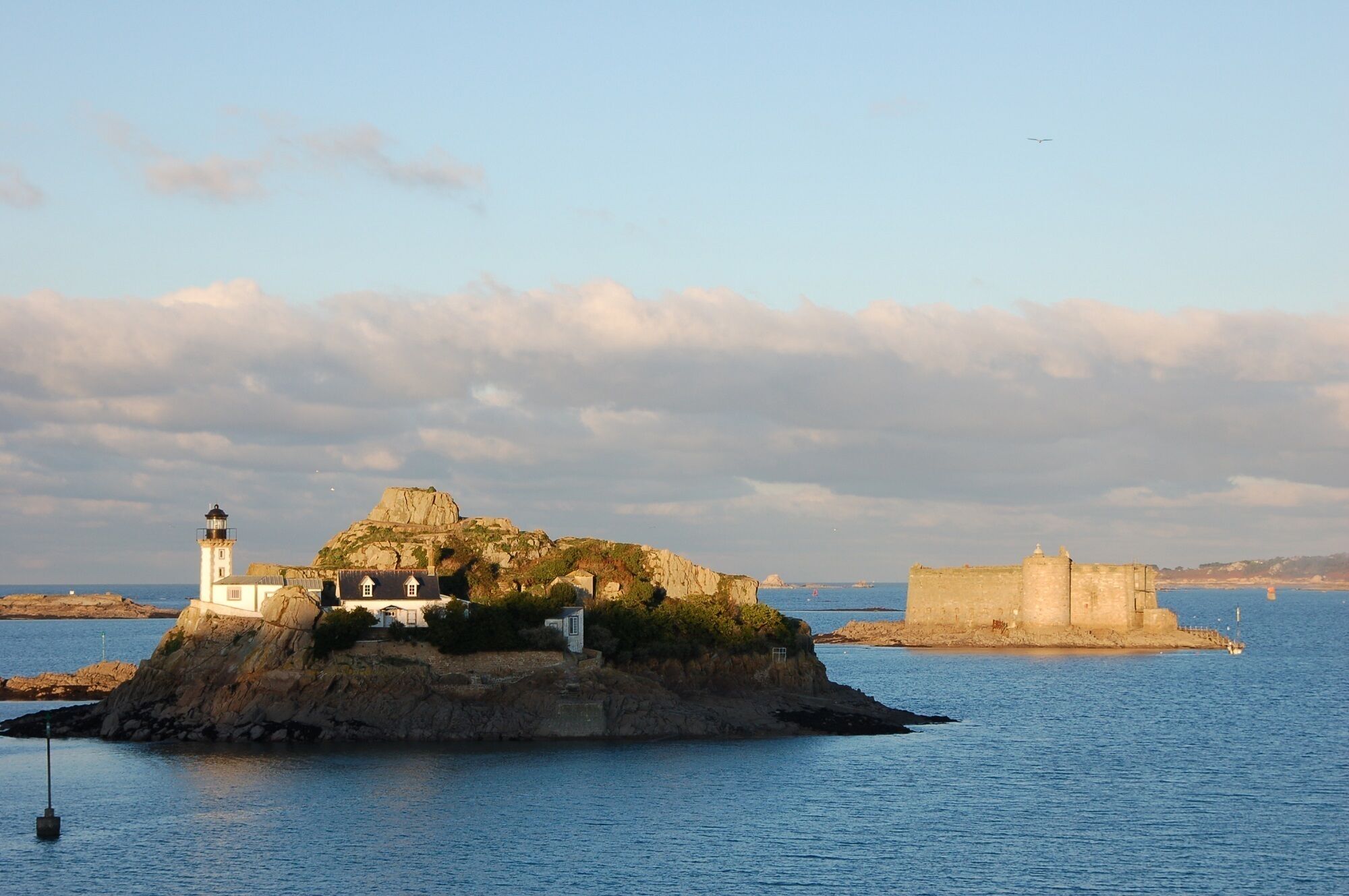 A coastal island with a lighthouse, a small building, and a fort.