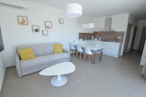 Un salon moderne comprenant un canapé, une table à manger et des chaises. On y trouve également un coin cuisine avec des placards et un plan de travail.