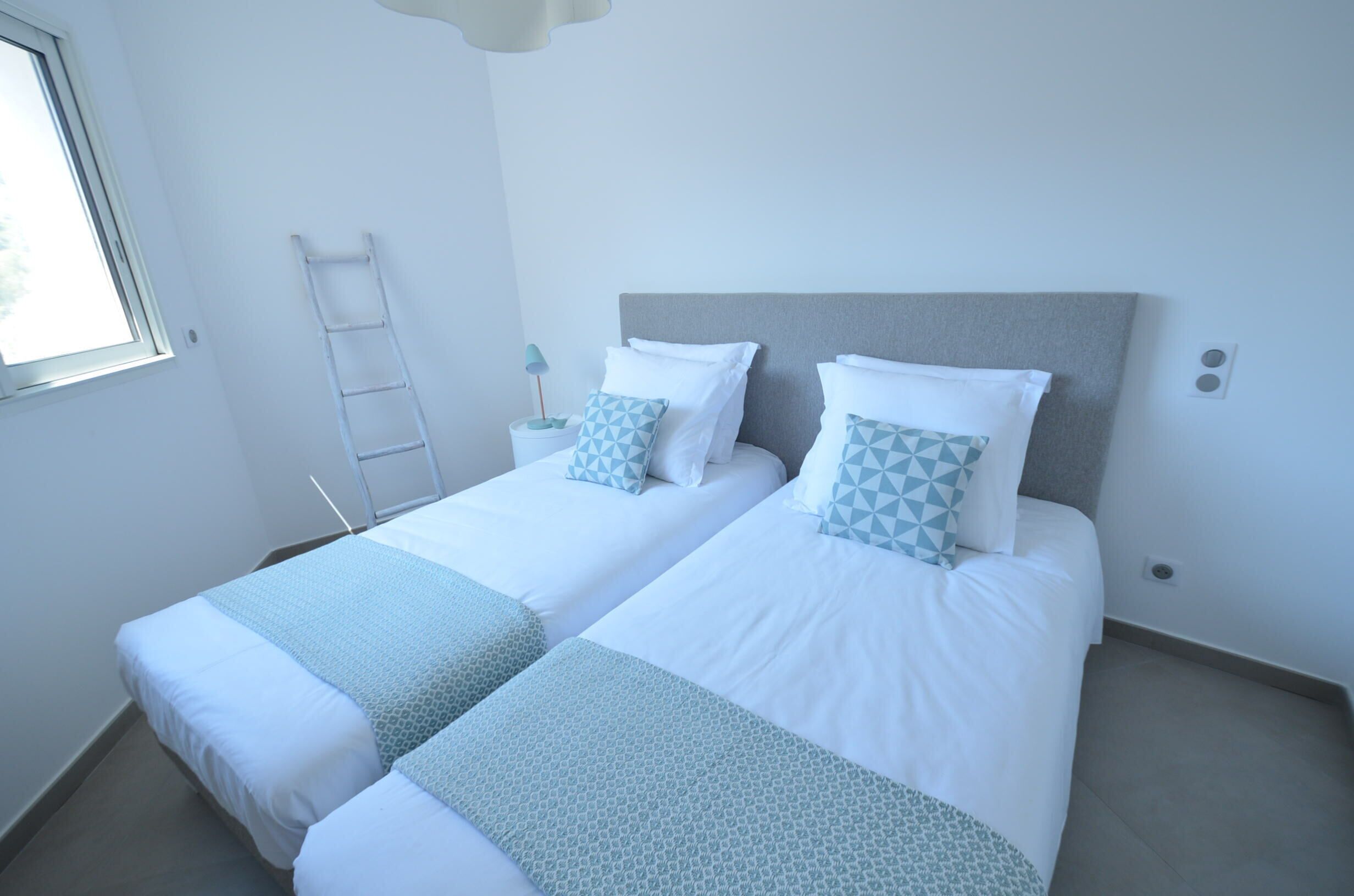 Une chambre double avec deux lits simples, une échelle, une table de chevet et une fenêtre.