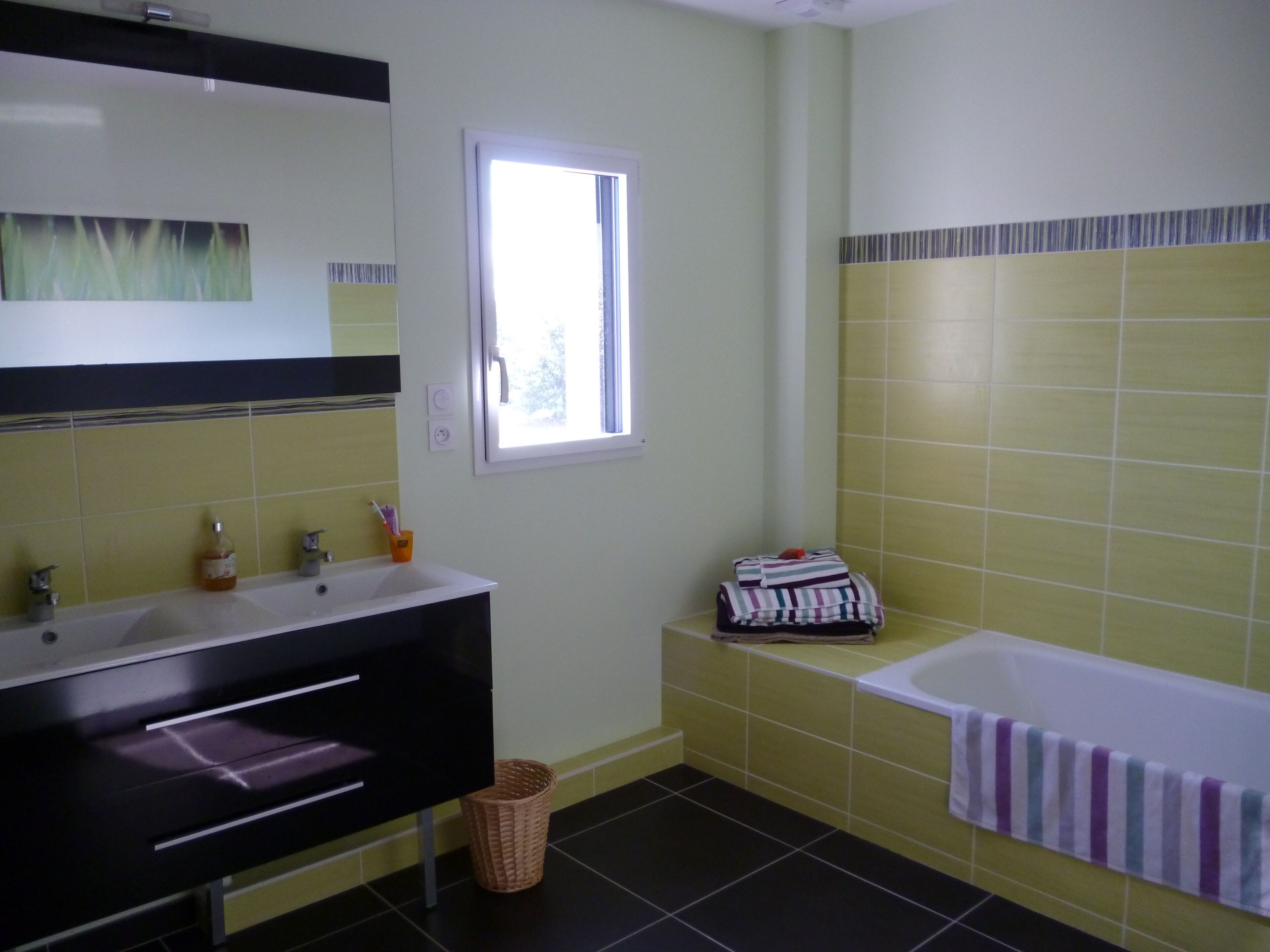Ein Badezimmer mit schwarzem Waschtisch, weißem Waschbecken, einem Spiegel, einem Fenster, einer Badewanne und einem Handtuchhalter.