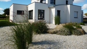 Une maison moderne à deux étages, avec une façade blanche, de grandes fenêtres et une allée gravillonnée.