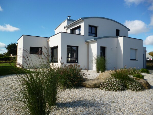 A modern two-story house with a white exterior, large windows, and a gravel driveway.