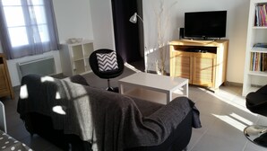 A modern living room with a sofa, a coffee table, a TV on a wooden cabinet, and a bookshelf.
