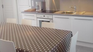 A modern kitchen with white cabinets, a stainless steel range hood, and a dining area with a polka dot tablecloth.