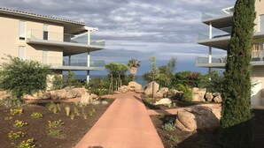 Un chemin mène à un bâtiment moderne doté de balcons qui offrent une vue sur un paysage rocheux et la mer.