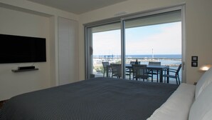 Une chambre avec un grand lit, un téléviseur fixé au mur et un balcon équipé d’une table et de chaises.