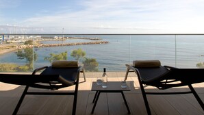 Un balcon avec deux fauteuils et une table, donnant sur une marina où sont amarrés des bateaux, ainsi que sur une digue rocheuse.
