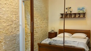 A bedroom with a wooden bed, a large mirror, a nightstand, and a wall-mounted shelf with decorative items. - 3-STAR HOUSE IN LA COTINIERE, 50 M FROM THE FISHING PORT (saint pierre d oleron)