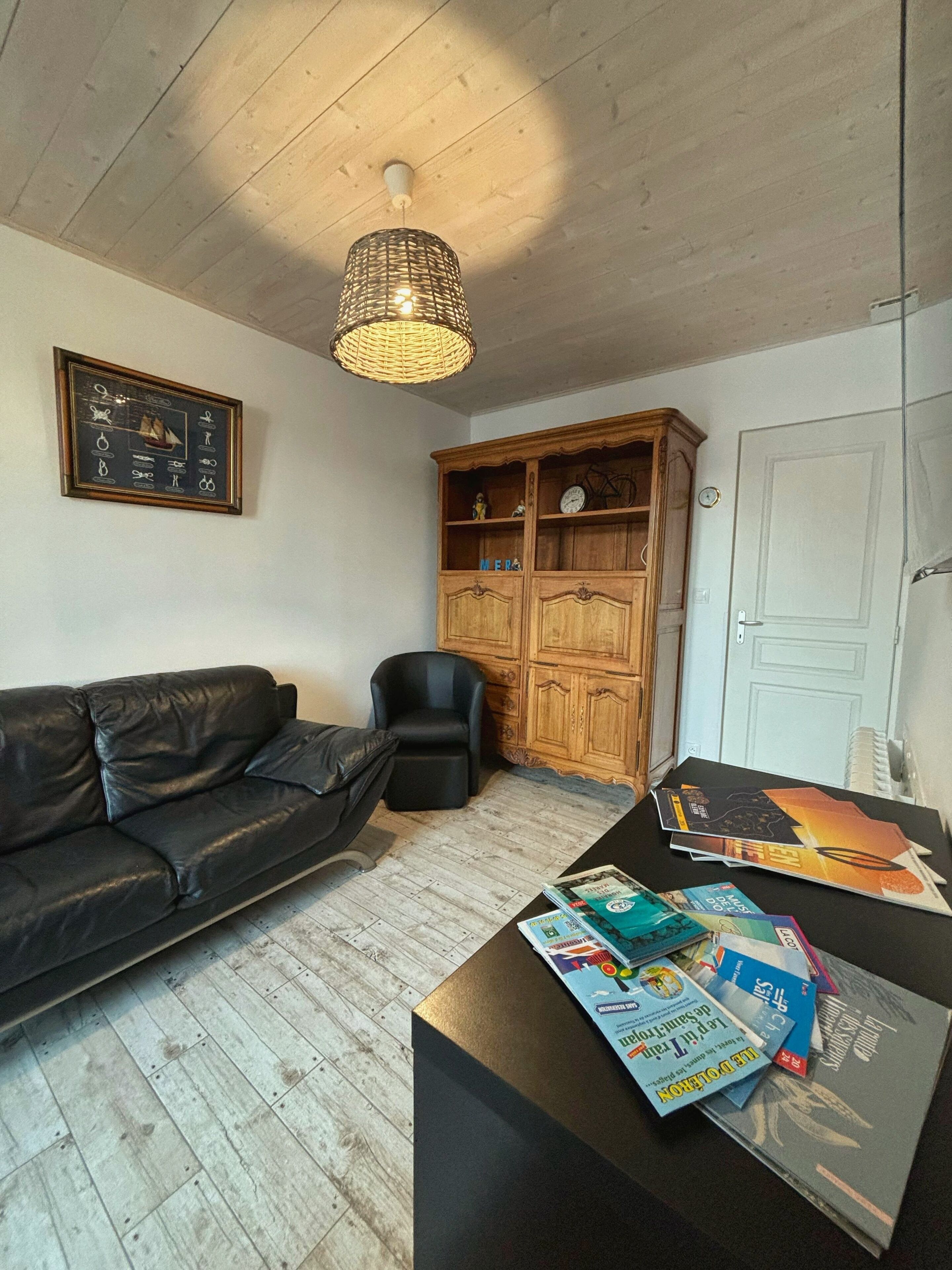 Un salon avec un canapé en cuir noir, un meuble en bois et une table sur laquelle sont posés des magazines.